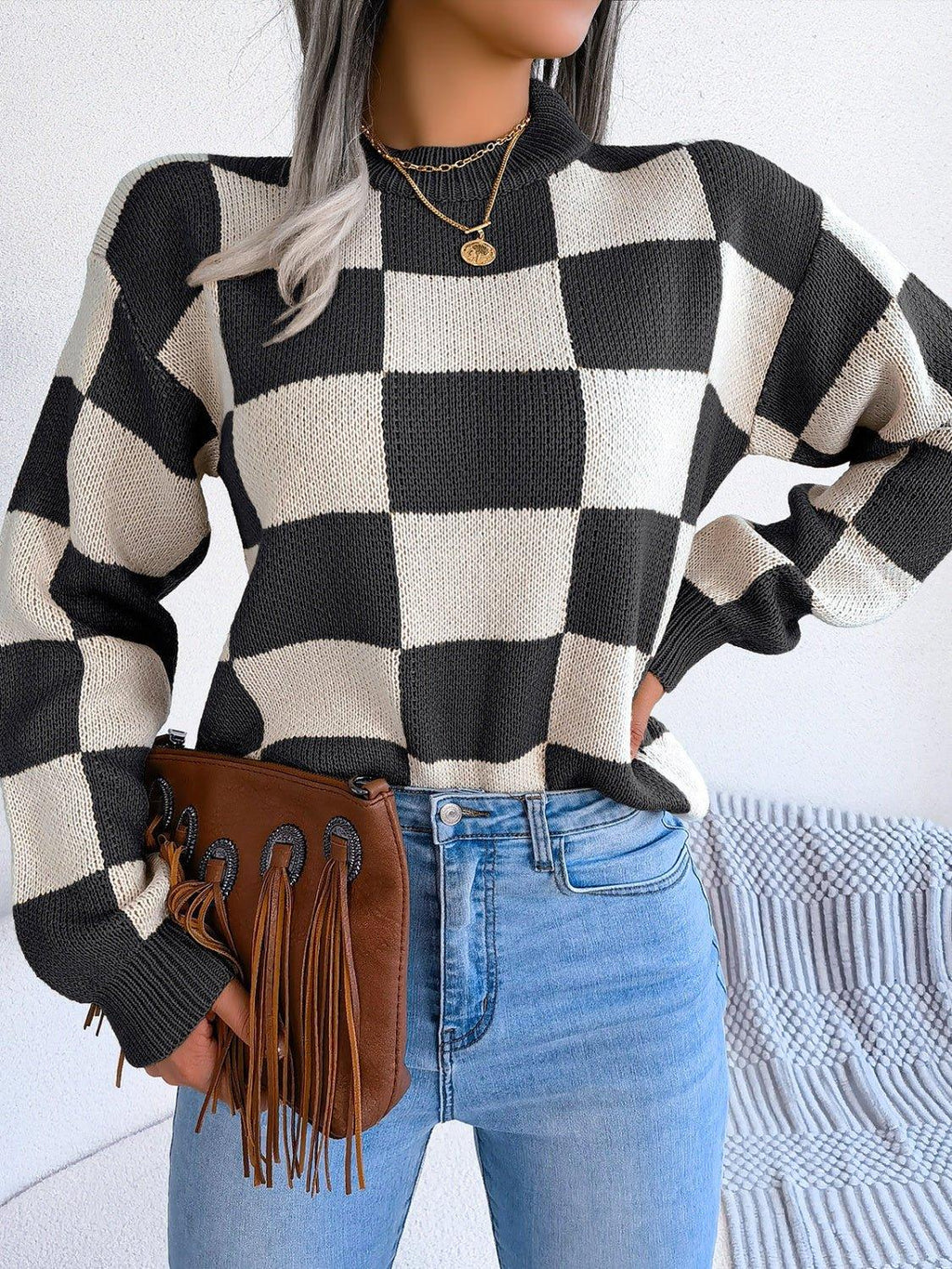 Woman posing with hands on hips in a checkerboard sweater and blue jeans.