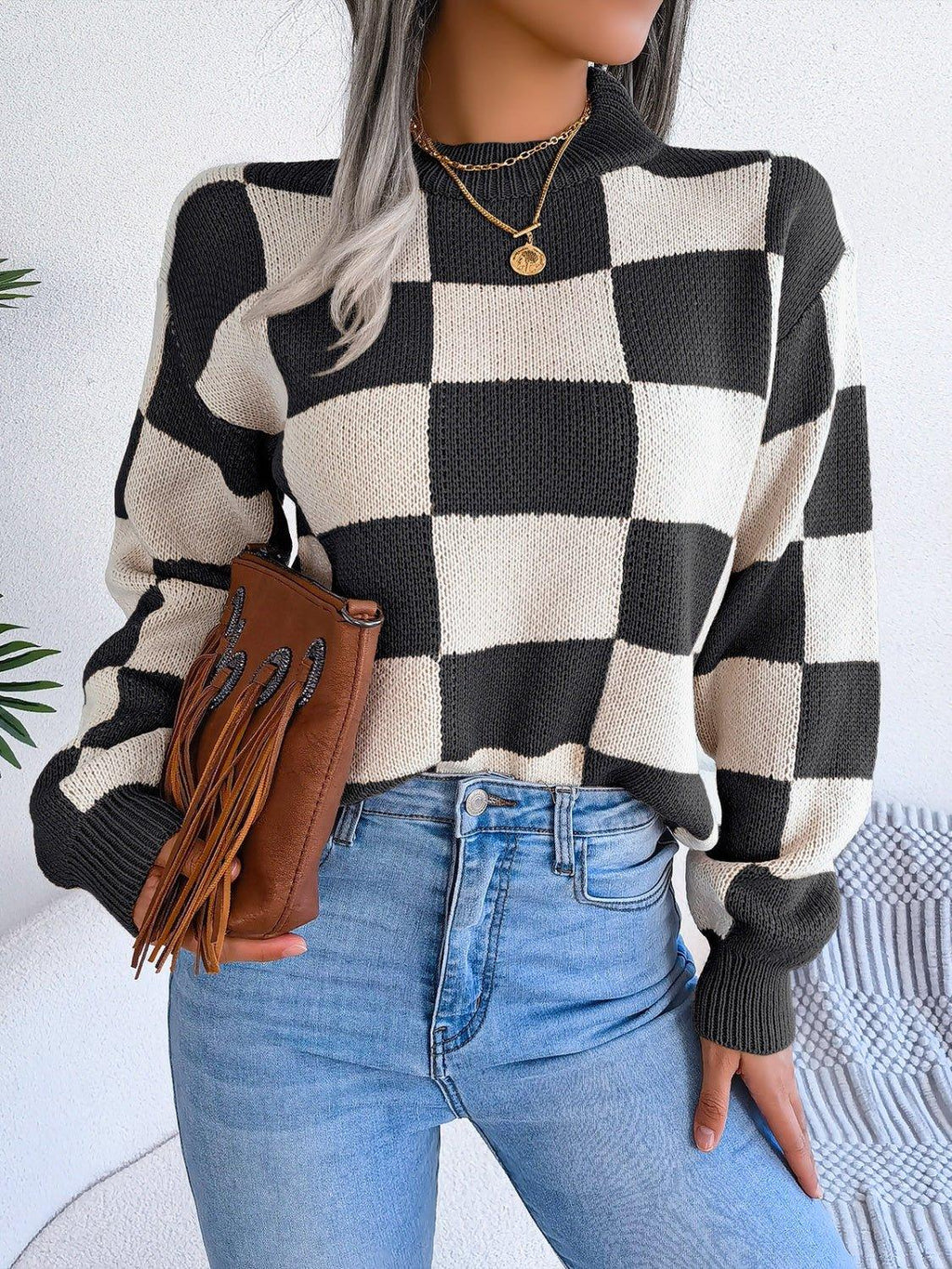 Woman holding a brown fringed clutch while wearing a checkerboard sweater.