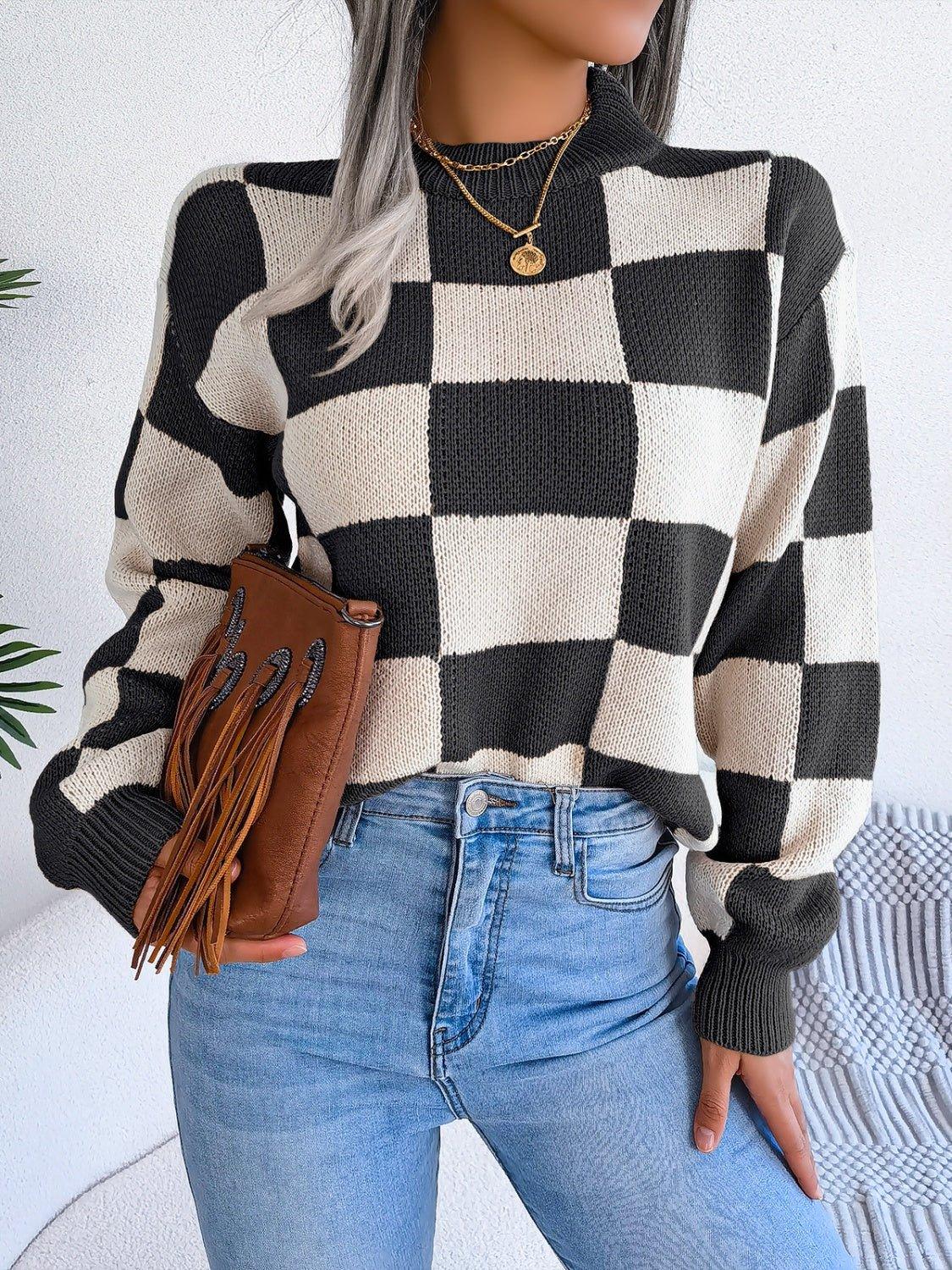 Woman holding a brown fringed clutch while wearing a checkerboard sweater.