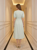 Rear view of a woman in a light green and white striped midi dress with puff sleeves and a smocked waist, standing in a hallway.