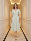 Woman wearing a light green and white striped midi dress with puff sleeves and a smocked waist, standing in a hallway.