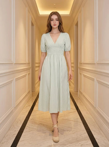 Woman wearing a light green and white striped midi dress with puff sleeves and a smocked waist, standing in a hallway.