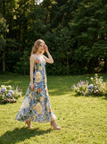 Woman wearing a fruit and floral print maxi dress, standing in a grassy field in a garden setting.