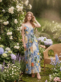 Woman wearing a maxi dress with a fruit and floral print, posing in a garden with white roses.