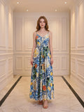 Woman wearing a full-length maxi dress with a colorful fruit and floral print, standing in a hallway.