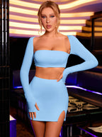 Woman posing in a light blue long-sleeve cropped top and a fitted skirt with a thigh-high slit.