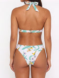 Back view of a woman wearing a white bikini with a tropical floral print, showing the adjustable closure of the halter top and bikini bottoms.