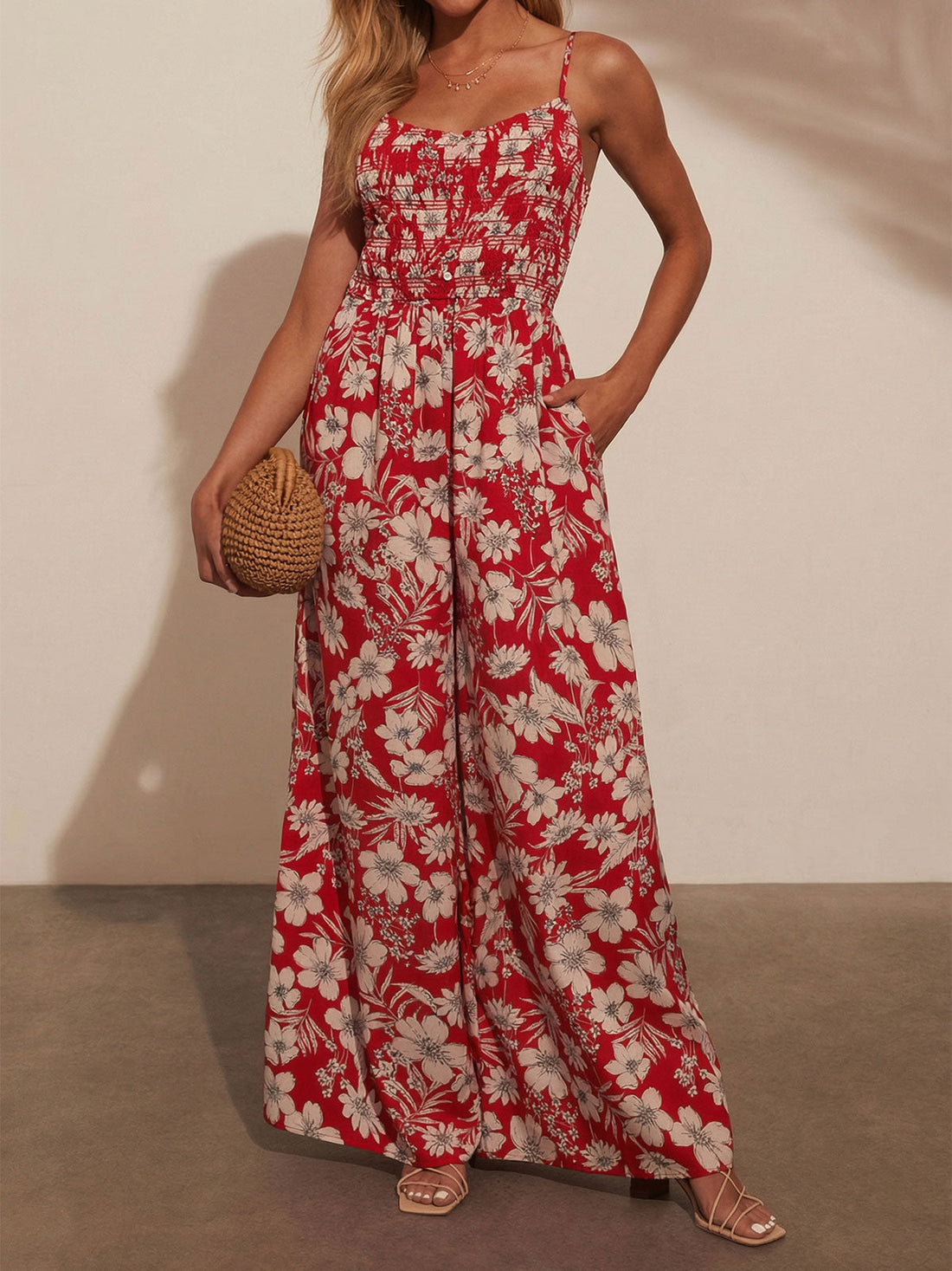 Woman wearing a red floral print wide-leg jumpsuit with a smocked bodice and spaghetti straps.