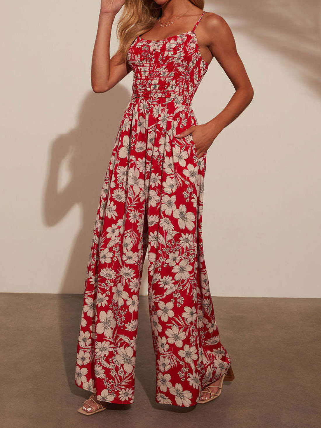 Woman wearing a red floral print wide-leg jumpsuit with a smocked bodice and spaghetti straps.