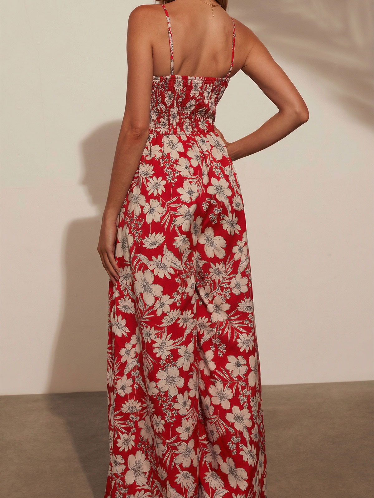 Back view of a woman in a red floral print wide-leg jumpsuit with a smocked bodice.