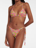 Woman wearing a pink, yellow, and blue floral print triangle bikini top with adjustable halter ties