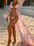Woman wearing a floral print maxi kimono over a bikini on a sandy beach.