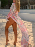 Back view of a woman in a sheer floral print kimono with a long flowing train on the beach.
