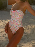 Woman wearing a strapless floral print one-piece swimsuit on a sandy beach.