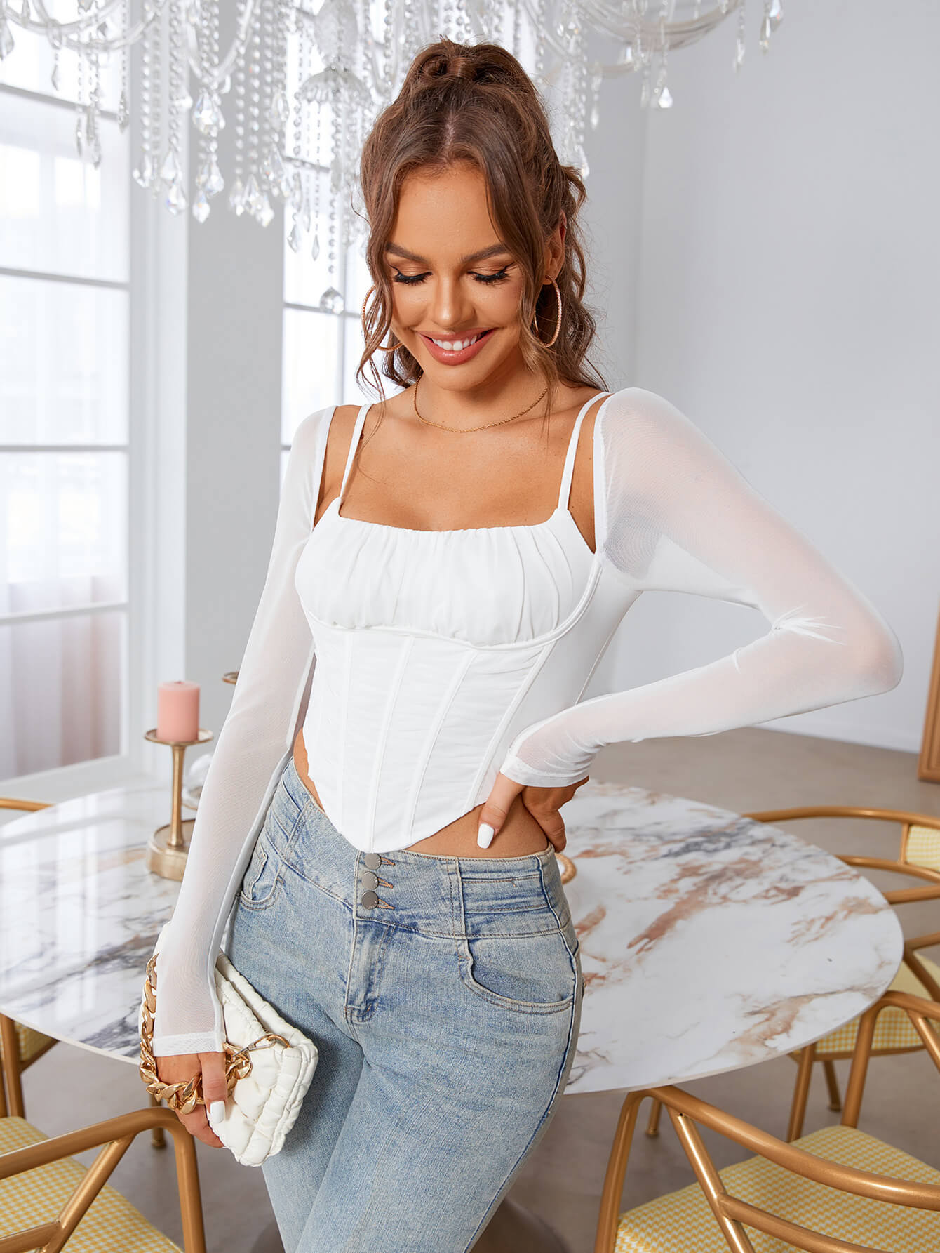 Woman smiling and posing in a white ruched bust corset top with sheer long sleeves