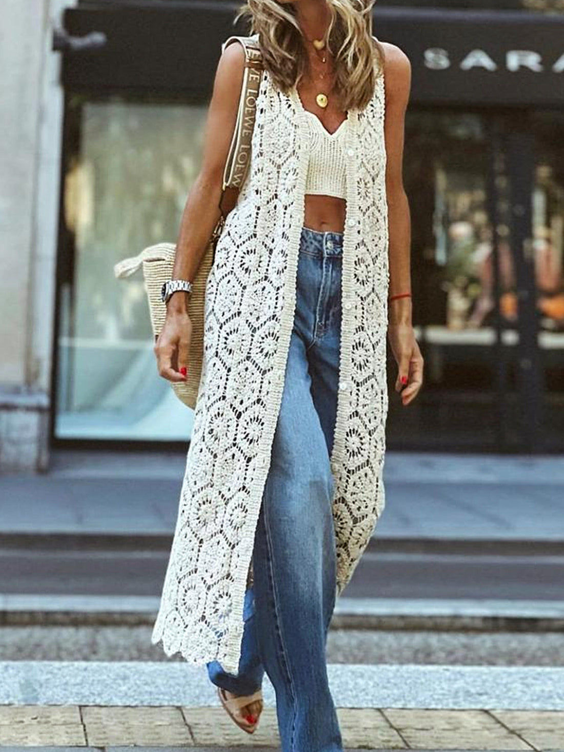 Woman wearing a white open-knit maxi vest over a crop top and wide-leg jeans.