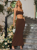 Woman holding a small white handbag, wearing a brown halter neck crop top and a brown maxi skirt with a mermaid hemline.