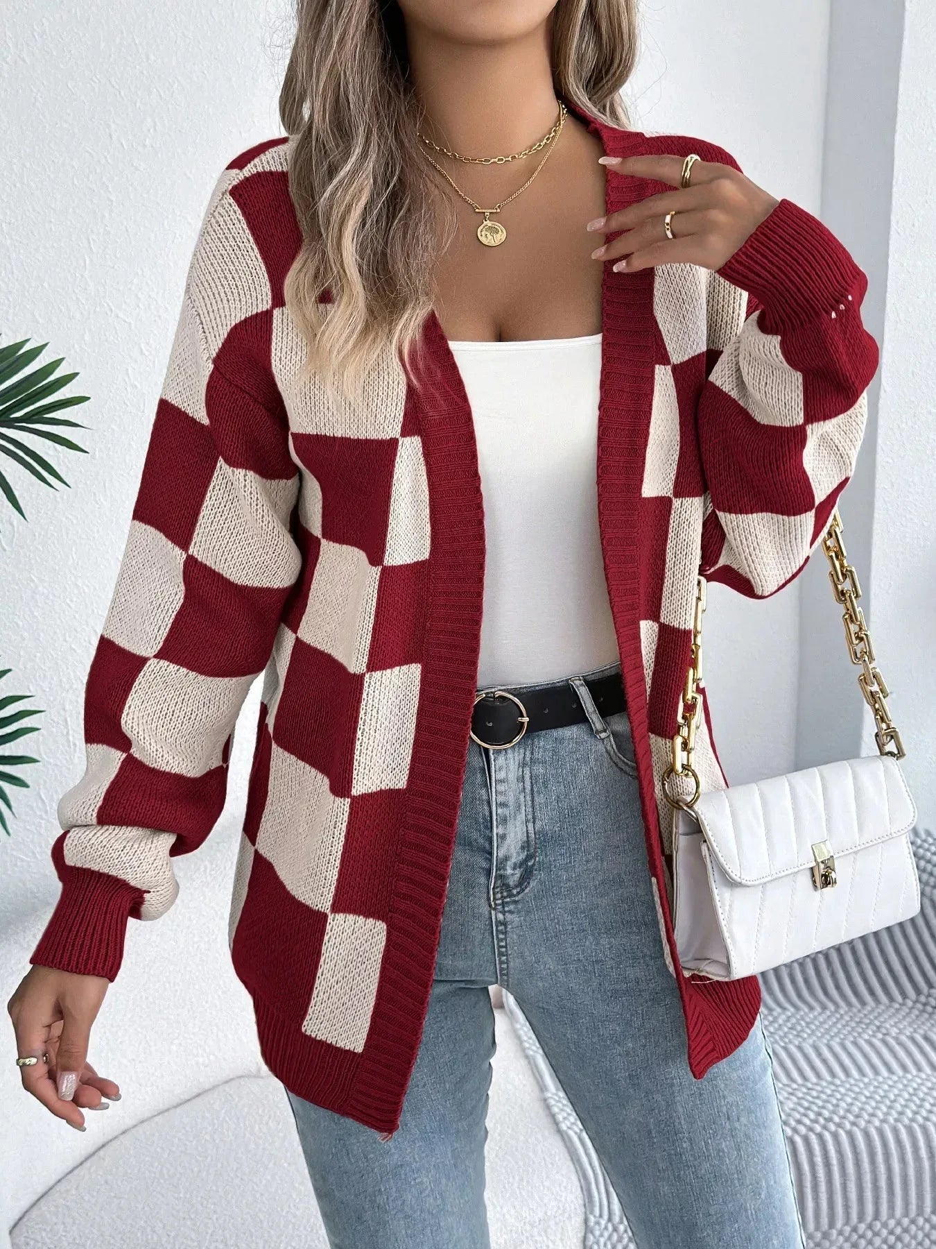 Woman wearing a red and cream checkerboard knit cardigan, white tank top, blue jeans, and gold jewelry. Main image