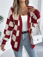 Woman wearing a red and cream checkerboard knit cardigan, white tank top, blue jeans, and gold jewelry.