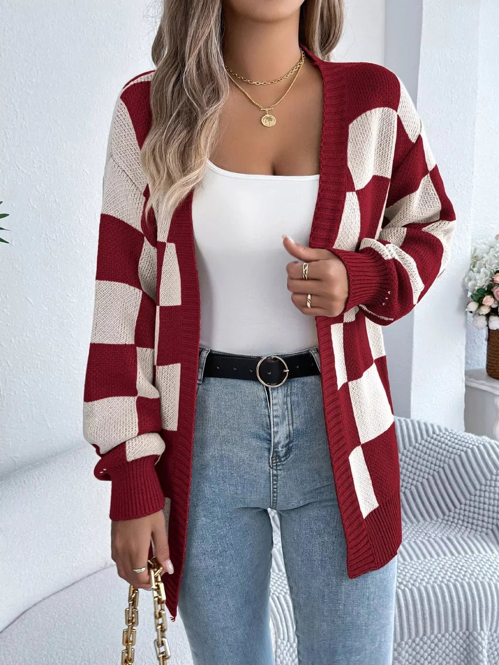 Woman in a red and cream checkerboard knit cardigan with a white tank top and blue jeans.