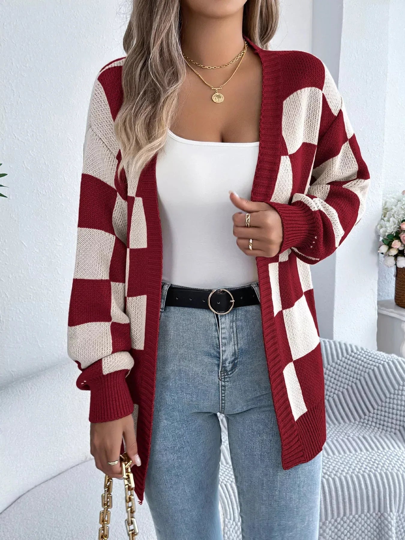 Woman in a red and cream checkerboard knit cardigan with a white tank top and blue jeans.