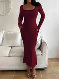 Woman in a long-sleeved, form-fitting, scoop neck red maxi dress standing in front of a white sofa.