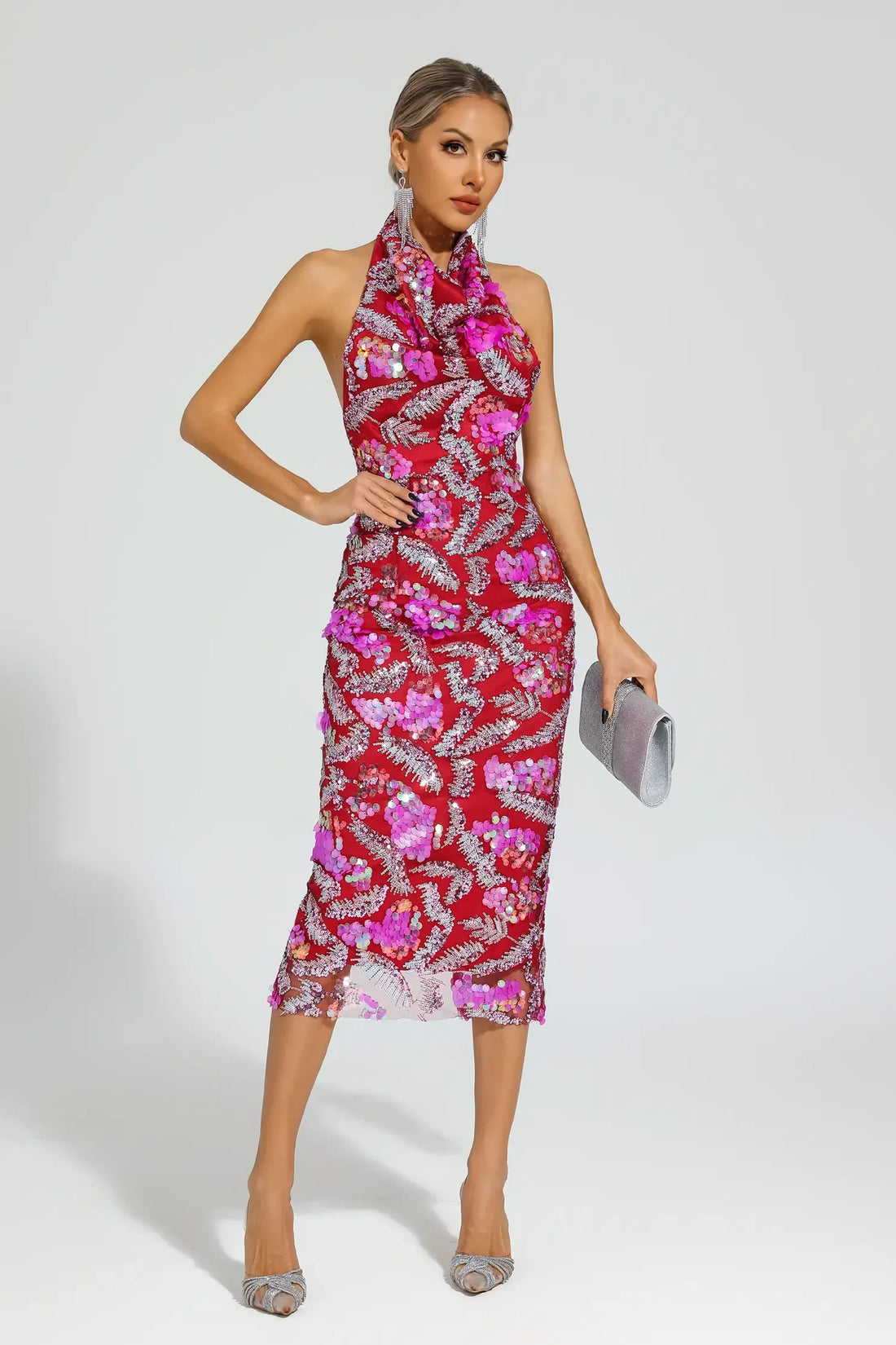 A model wearing a pink and red floral halter midi dress with sequin appliques, paired with silver accessories and shoes.
