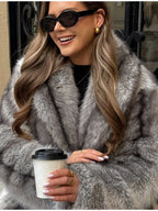 Woman sitting on a ledge wearing a grey faux fur coat and black boots