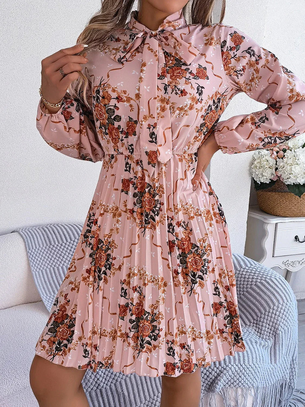 Model posing in a pink floral print midi dress with a bow neckline and pleated skirt
