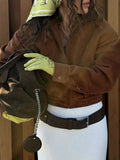 Close-up of a woman wearing a brown corduroy jacket, holding a bag and wearing light green lace gloves.