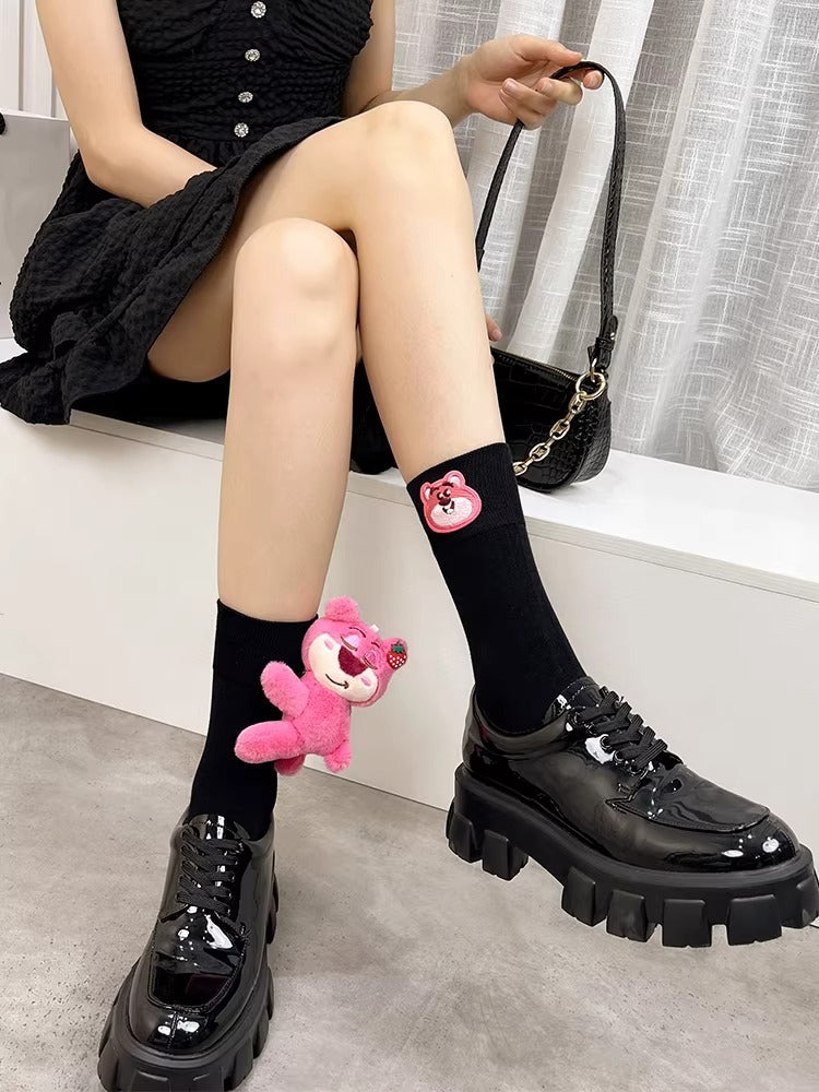 Close-up of black knee-high socks with a pink plush bear charm attached to the side.