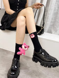 Person wearing black knee-high socks with a pink plush bear charm and black platform shoes.
