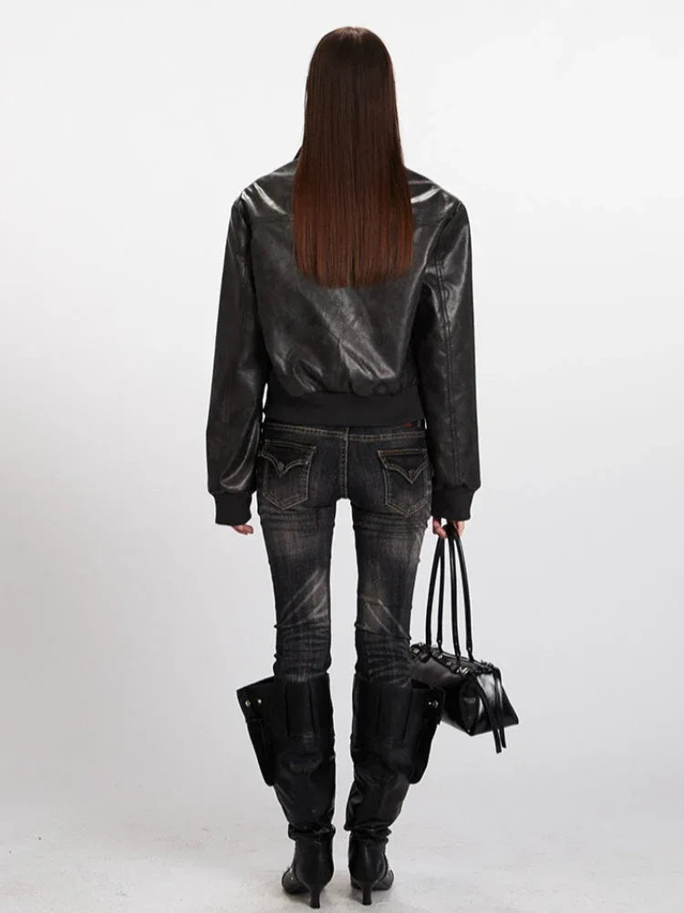 Back view of a woman in a black faux leather bomber jacket, black jeans, and black boots.