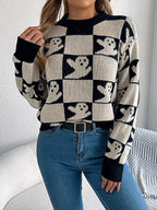 Front view of a woman wearing a black and cream checkerboard knit sweater with ghost print, blue jeans, and a black belt.