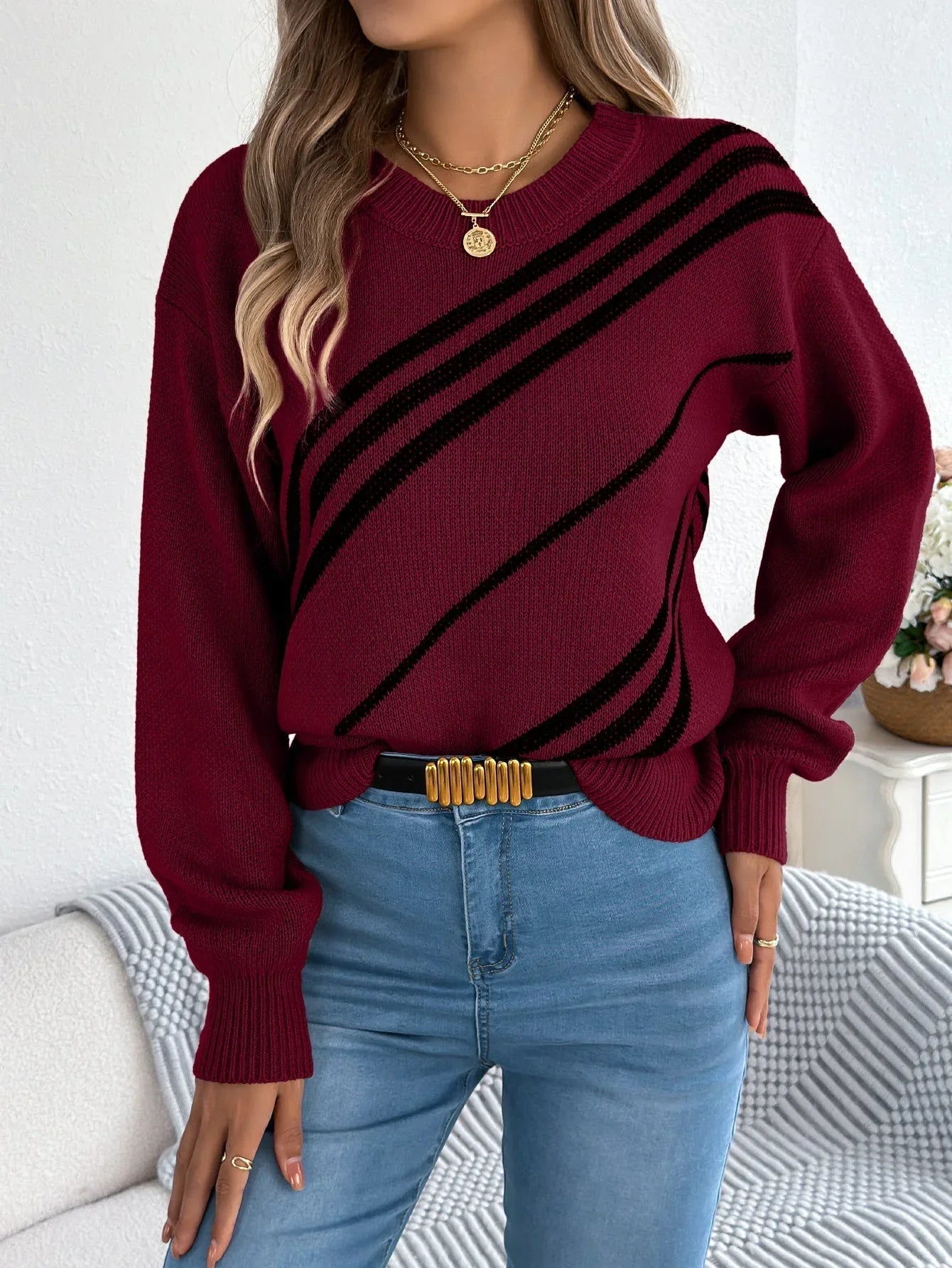 Woman wearing a maroon knit sweater with black diagonal stripes and blue denim jeans. Main image