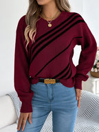 Close-up of a woman wearing a maroon knit sweater with black diagonal stripes and a gold pendant necklace.