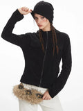 Woman adjusting her black beanie while wearing a black zip-up fleece jacket and white pants.