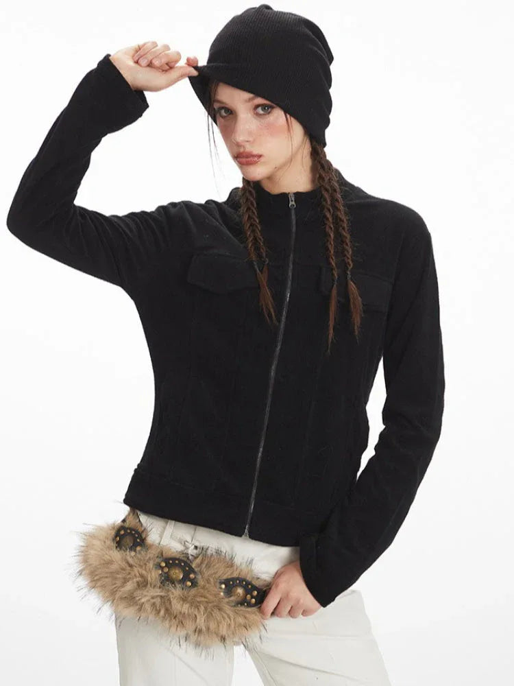 Woman adjusting her black beanie while wearing a black zip-up fleece jacket and white pants.