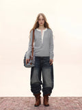 Woman wearing a light grey long-sleeved knit sweater with a white contrast neckline and button-up placket, carrying a denim crossbody bag and wearing distressed denim jeans and brown boots.