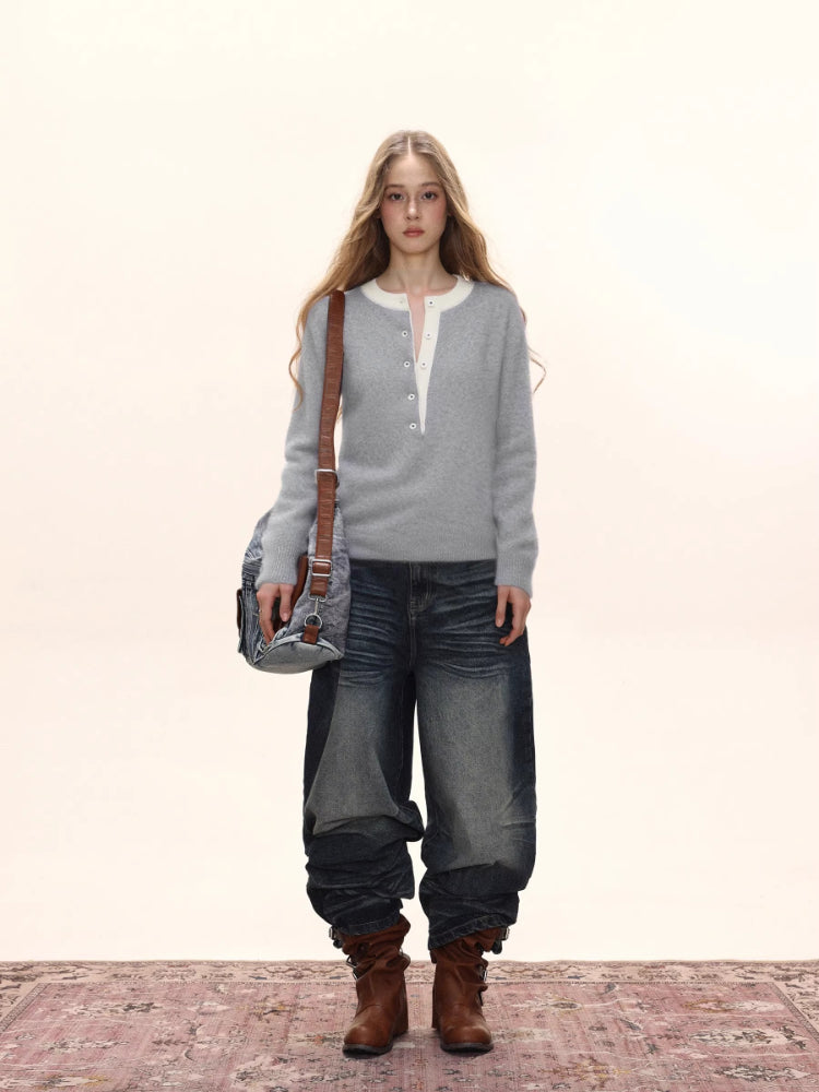 Woman wearing a light grey long-sleeved knit sweater with a white contrast neckline and button-up placket, carrying a denim crossbody bag and wearing distressed denim jeans and brown boots.