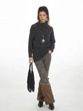 Full body shot of a woman in a charcoal grey knit tunic sweater paired with patterned leggings and furry leg warmers.