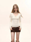 Front view of a woman in a cream long-sleeve top with lace trim and a bow detail, and brown shorts.