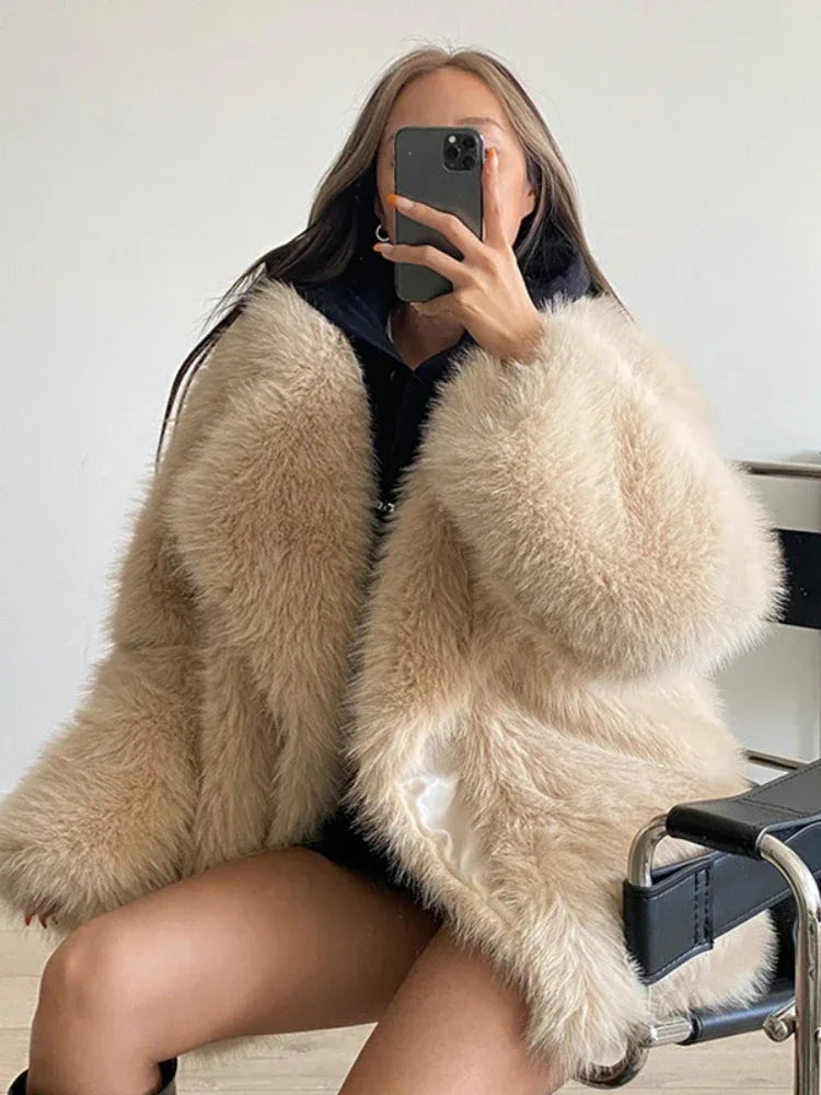 Woman wearing a cream turtleneck and a brown shaggy faux fur coat standing with arms crossed.