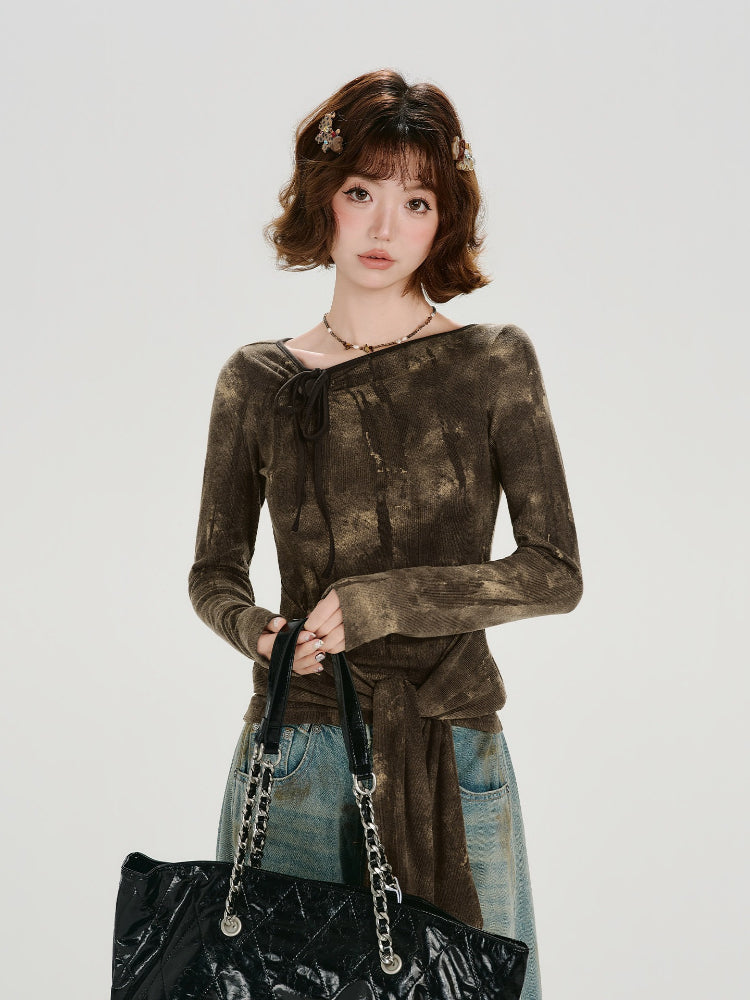 Woman wearing a long-sleeve brown tie-front top with a tie-neck detail and acid wash effect, paired with light-wash wide-leg jeans.