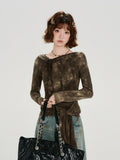 Front view of a woman in a long-sleeve brown tie-front top with a tie-neck detail and acid wash effect, holding a black quilted tote bag.