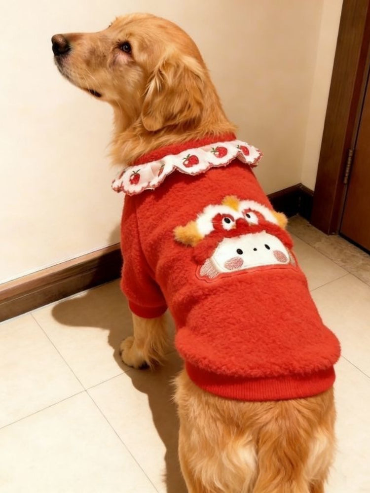 Golden Retriever dog wearing a red fleece dog sweater with a white ruffled collar and embroidered strawberry pattern, facing left