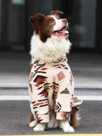 Dog wearing a cream-colored fleece jacket with a black and red geometric pattern.