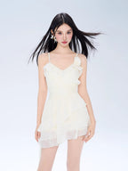 Woman wearing a cream-colored mini dress with spaghetti straps and ruffle detailing.