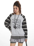 Close-up of a model wearing a grey graphic print sweatshirt with striped sleeves.