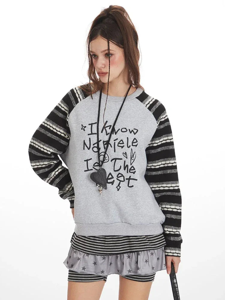Close-up of a model wearing a grey graphic print sweatshirt with striped sleeves.